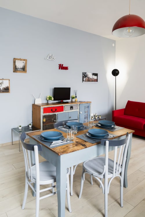 Modern dining room in LikeHome Mentessi apartment, Ferrara with set table, white chairs, red pendant light and living area
