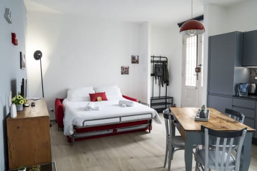 Modern studio apartment in Ferrara with red sofa bed, dining table, kitchenette, and city view from door