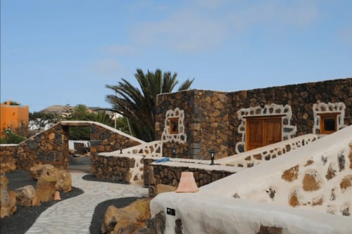 Patio del Hotel Rural El Cabo con arquitectura de piedra, barandillas blancas, puertas de madera y palmera en Villaverde, España