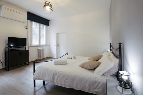 Modern bedroom with white linens, black metal bed frame, TV, and contemporary furnishings in Ferrara apartment