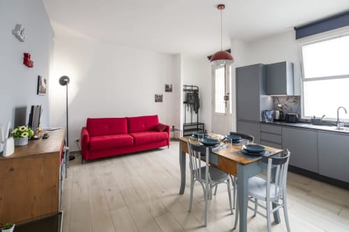 Modern Ferrara apartment with red sofa, dining table, gray kitchen, and pendant lighting - LikeHome Mentessi