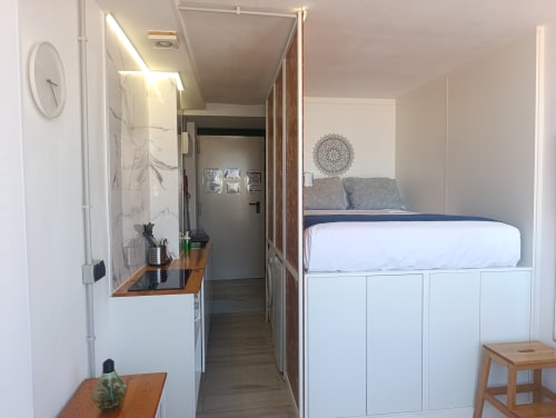 Dormitorio de estudio moderno en Sevilla con cama elevada, almacenamiento, escritorio de trabajo y entrada al baño