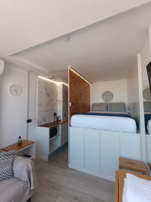 Moderno estudio en Sevilla con cama elevada, cocina americana, zona de estar con detalles de madera y blanco