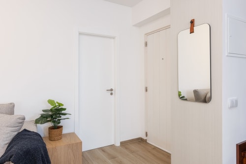 Entrada moderna do apartamento RB Algarve Vilamoura com portas brancas, assoalho em madeira, espelho, planta em vaso e tons cinzento