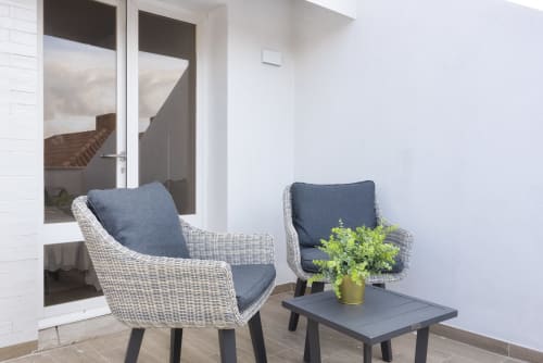 Espaço de estar moderno no RB Algarve Vilamoura com cadeiras de vime, almofadas azuis, plantas em vaso e portas de vidro com vista