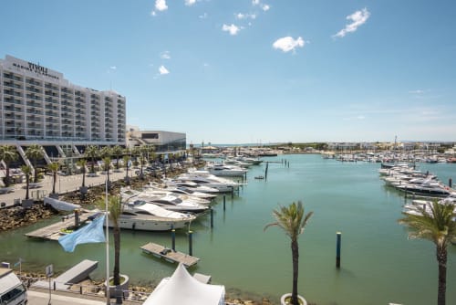 Marina do RB Algarve com iate de luxo atracado, palmeiras e edifício de apartamentos à beira-mar em Vilamoura, Portugal