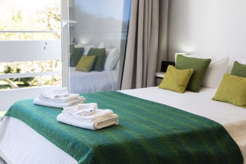 Quarto espaçoso no RB Algarve Vilamoura com camas gêmeas, roupa de cama verde, almofadas amarelas e varanda com vista para o jardim