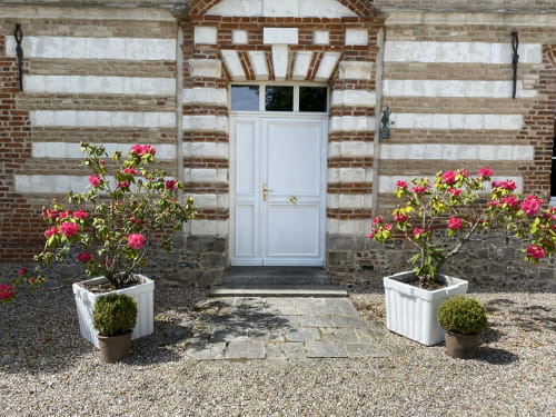 Entrée de la Maison Nolette avec porte blanche, roses roses en bacs, façade en brique et cour gravillonnée à Noyelles sur Mer