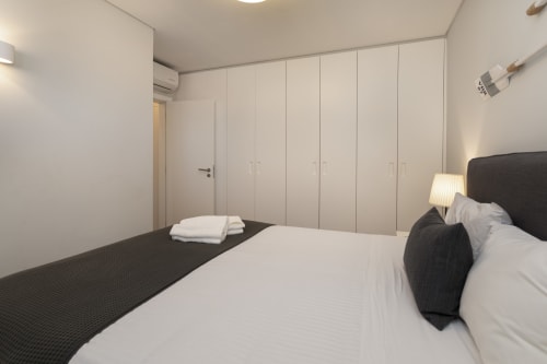 Quarto moderno com cama de casal, cabeceira preta, roupa de cama branca, guarda-roupa do chão ao teto e ar condicionado no RB Algarve