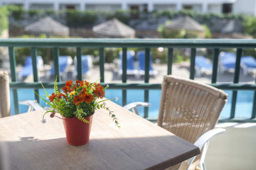 Varanda com vista para a piscina no RB Algarve Albufeira com flores vermelhas em vasos e espreguiçadeiras voltadas para a piscina do resort