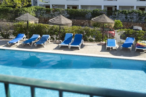 Piscina do hotel RB Algarve com espreguiçadeiras azuis, guarda-sóis e edifício branco em Albufeira, Portugal