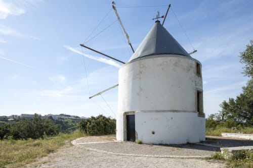 Moinho branco histórico com telhado cônico preto no interior do Algarve, Portugal