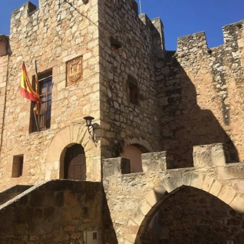 Castillo medieval de piedra con bandera española, entrada abovedada y torres almenadas en Rustikalpuente