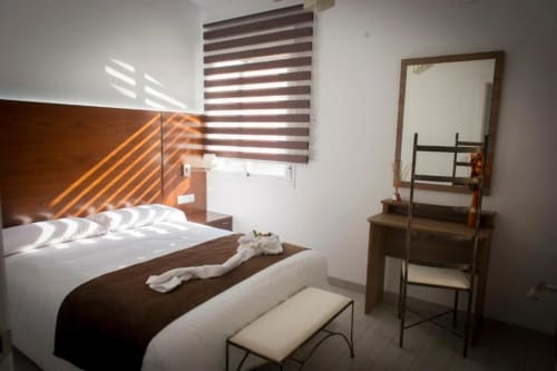 Modern bedroom at Complejo Turístico Retiro del Teatro with white bedding, wooden headboard, striped blinds, mirror, and