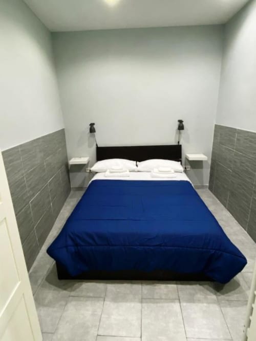 Modern bedroom at Neapolis Tecnotourist with blue comforter, black bed frame, and gray tile accents