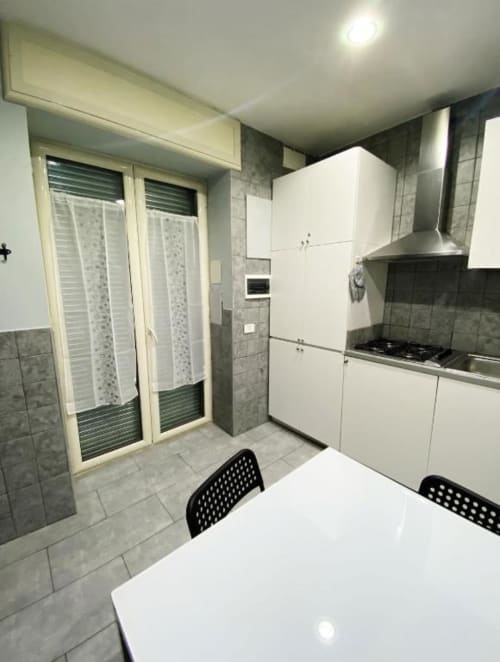 Modern kitchen at Neapolis Tecnotourist B&B in Italy with white cabinets, gas stove, and dining table by patio doors