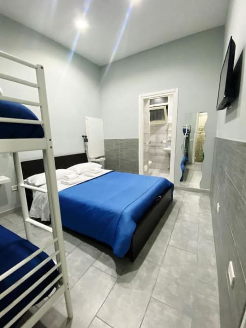 Modern bedroom at Neapolis Tecnotourist with blue bedding, white bunk beds, tiled flooring, and ensuite bathroom