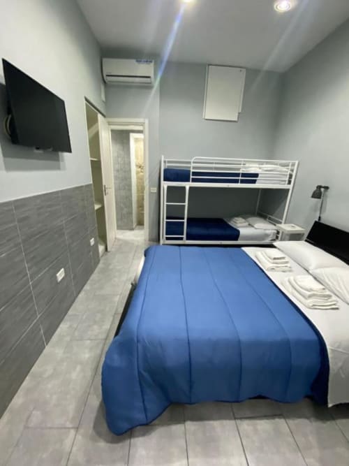 Modern dormitory room at Neapolis Tecnotourist with bunk beds, blue bedding, wall-mounted TV, and en-suite bathroom.
