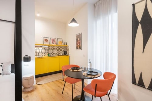 Modern Suite Maradona BnB dining area in Naples with yellow kitchen, round black table, orange chairs, and contemporary