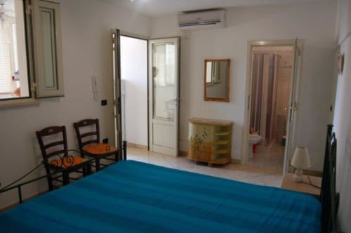Camera ampia a Santa Cesarea Vacanze con letto blu, sedie in legno, specchio e accesso alla vista del giardino in Italia