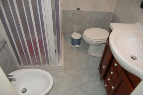 Bagno dell'appartamento a Santa Cesarea Terme con toilette, bidet, lavabo, tenda doccia e pavimento piastrellato