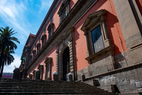 Neapolitan palazzo facade with red brick, arched windows, and grand staircase at Suite Maradona in Naples, Italy