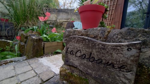 Patio du jardin aux Troglos de Beaulieu avec jardinière rustique en bois, fleurs roses et pot rouge à Beaulieu-lès-Loches.
