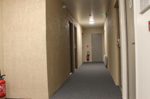 Couloir d'hôtel au Libre Hôtel à La Vespière avec murs beige, moquette grise, portes et extincteur