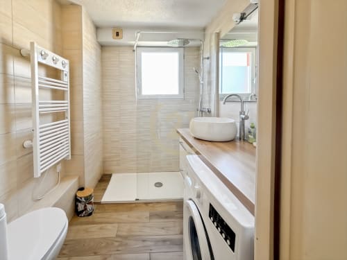 Salle de bain moderne avec douche à l'italienne, vasque blanche, porte-serviettes et lave-linge dans l'appartement de L'Île-Rousse