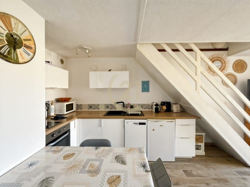Cuisine-salle à manger duplex moderne avec armoires blanches, comptoirs en bois et escalier, appartement L'Île-Rousse près de la plage