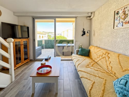 Salon moderne d'un duplex à L'Île-Rousse avec canapé jaune, TV et portes vitrées donnant sur une terrasse ensoleillée