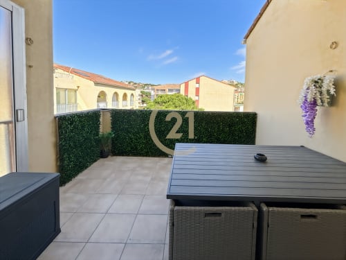 Terrasse duplex moderne avec table à manger, fleurs de glycine et enseigne Century 21 surplombant L'Île-Rousse