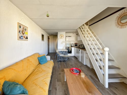 Appartement duplex moderne à L'Île-Rousse avec canapé jaune, table en bois, escalier blanc, cuisine et vue sur la ville