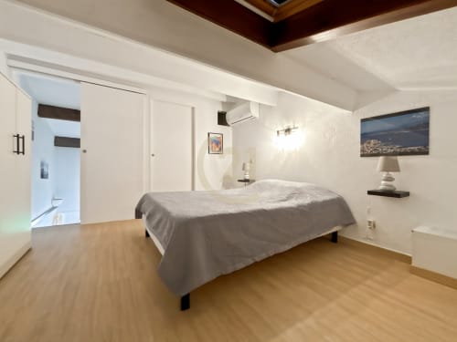 Chambre moderne du duplex à L'Île-Rousse avec parquet, lit gris, murs blancs, climatisation et décoration artistique ville