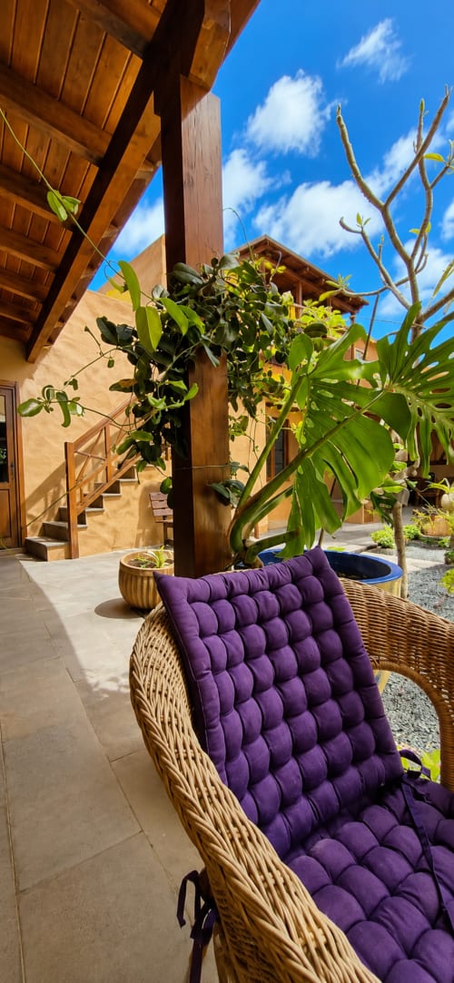 Fauteuil en rotin rembourré de violet sur la terrasse, entouré de plantes luxuriantes et de poutres en bois à Sara & Gino Fuerteventura, Corralejo