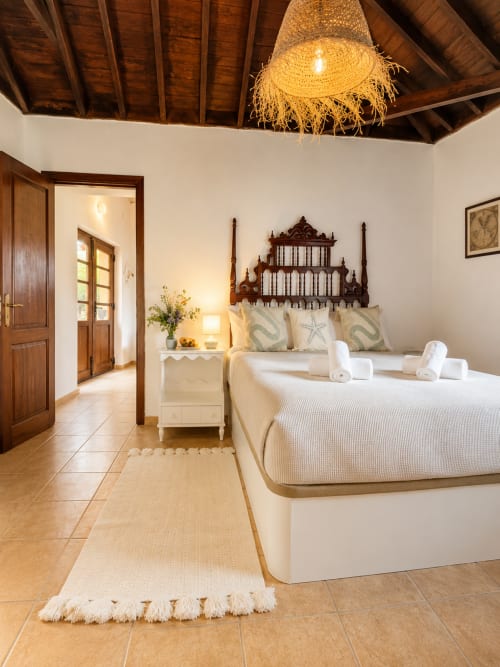 Chambre spacieuse avec lit à baldaquin en bois ouvragé, draps blancs, poutres apparentes et carrelage en terre cuite