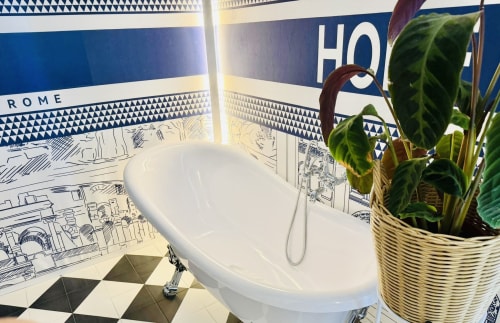 Lussuosa vasca da bagno bianca nella Superior Family Room del St Mary Major Loft Roma, con pareti in piastrelle blu decorative e pianta in vaso