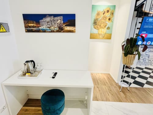 Spazioso angolo di lavoro in camera d'hotel con scrivania, sedia turchese, quadri di girasoli e stampa della Fontana di Trevi a St Mary Major Loft Roma