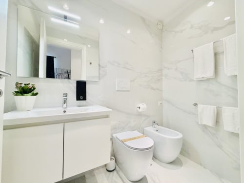 Bagno moderno con pareti in marmo, sanitari bianchi, water, bidet e lavabo con specchio al St Mary Major Loft di Roma