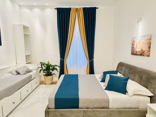 Camera tripla presso St Mary Major Loft a Roma con letto queen, accenti turchesi, tende blu scuro, arredamento bianco e vista sul giardino