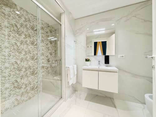 Bagno moderno nel St Mary Major Loft Roma con pareti in marmo, vanità bianca, box doccia in vetro e specchio illuminato