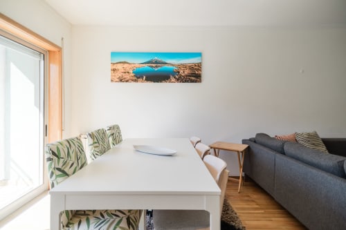 Sala de jantar de apartamento moderno com mesa branca, almofadas com padrão verde, sofá escuro, piso de madeira e paisagem montanhosa