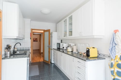 Cozinha branca moderna no apartamento EcoHost com bancadas de granito, eletrodomésticos e porta de madeira para o corredor