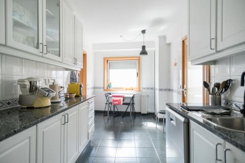 Cozinha moderna branca com bancadas de granito, área de refeições e janela com moldura de madeira no apartamento Gaia Beach&Golf EcoHost
