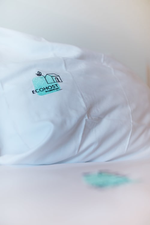 Toalha branca enrolada com logotipo turquesa EcoHost com amenidades de higiene veganas