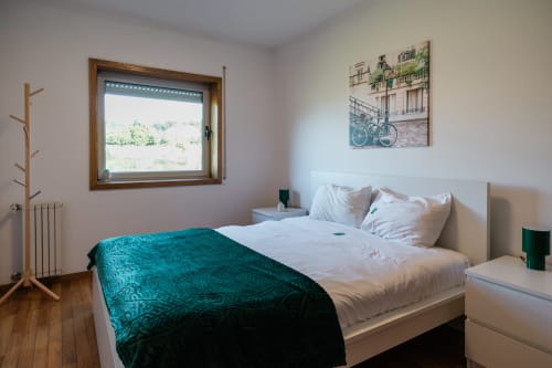 Quarto luminoso no apartamento EcoHost com cama queen, manta azul-petróleo, janela de madeira com vista para a zona rural e design moderno