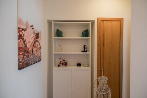 Interior moderno de apartamento com estante branca exibindo itens decorativos, arte de bicicleta vermelha vintage na parede, porta de madeira