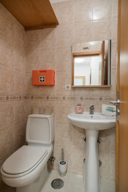 Banheiro EcoHost com pia de pedestal branca, vaso sanitário e kit de primeiros socorros no apartamento Gaia Beach&Golf