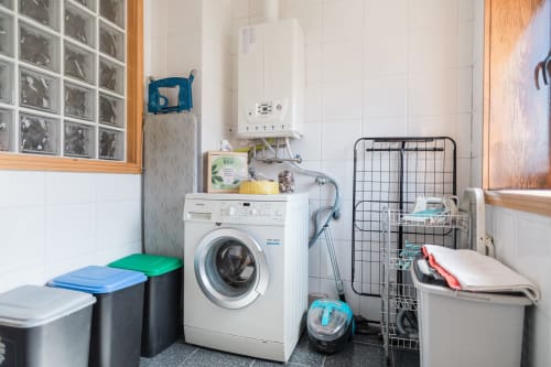 Sala de lavanderia na EcoHost com máquina de lavar, secadora, cestos de armazenamento e produtos de limpeza