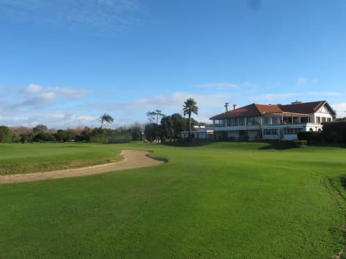 Amplos gramados verdes com caminho de terra levando à casa branca de dois andares, palmeira e céu azul na Gaia Beach&Golf EcoHost